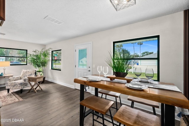 dining room featuring dark wood finished floors, visible vents, a healthy amount of sunlight, and a textured ceiling