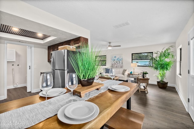 dining space featuring visible vents, baseboards, ceiling fan, dark wood finished floors, and a raised ceiling