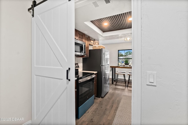 kitchen featuring stainless steel microwave, visible vents, a barn door, electric range oven, and a raised ceiling