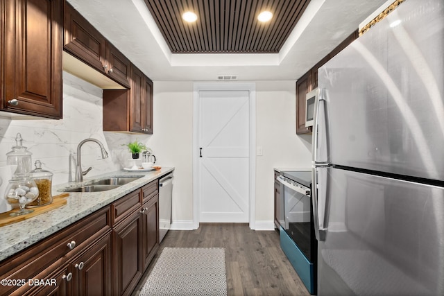 kitchen featuring tasteful backsplash, a sink, stainless steel appliances, a raised ceiling, and dark wood-style flooring