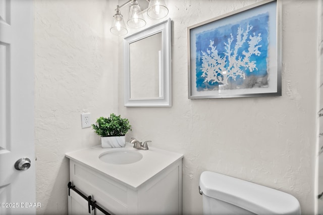 bathroom with toilet, vanity, and a textured wall