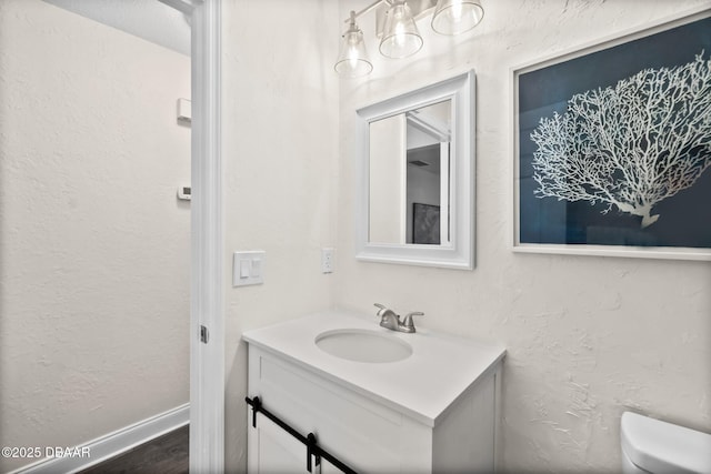 bathroom featuring vanity, wood finished floors, baseboards, toilet, and a textured wall