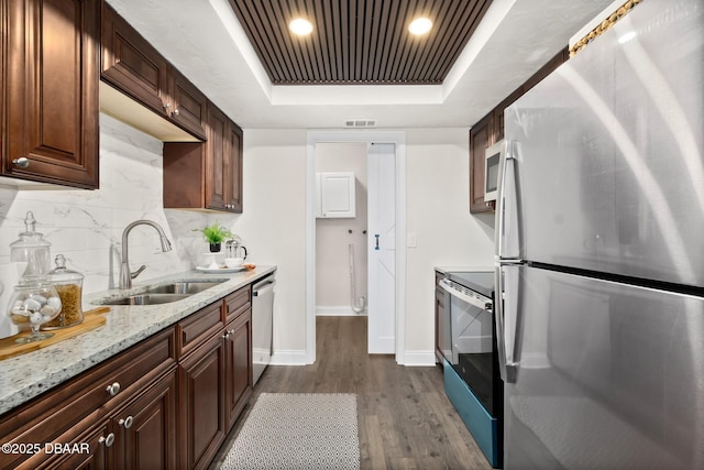 kitchen with appliances with stainless steel finishes, sink, decorative backsplash, a tray ceiling, and dark wood-type flooring