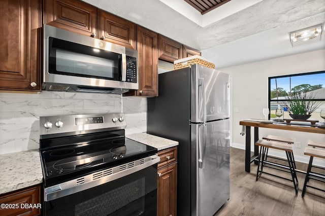 kitchen featuring tasteful backsplash, light stone counters, light hardwood / wood-style flooring, and appliances with stainless steel finishes