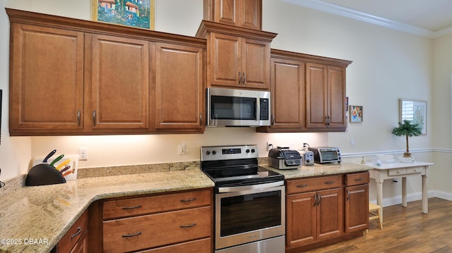 kitchen with brown cabinets, dark wood-style flooring, light stone countertops, stainless steel appliances, and ornamental molding