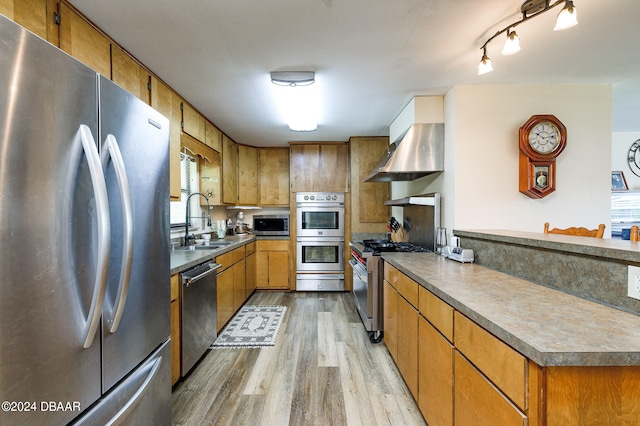 kitchen with stainless steel appliances, wall chimney exhaust hood, a sink, and brown cabinets