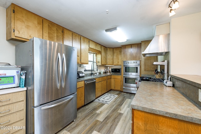 kitchen featuring a warming drawer, appliances with stainless steel finishes, light wood-style floors, a sink, and ventilation hood