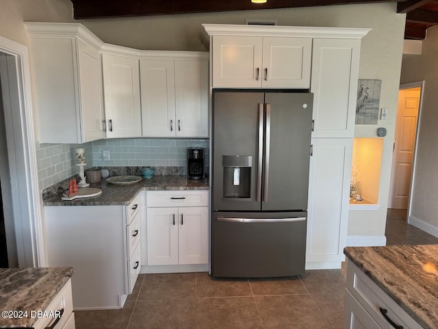 kitchen featuring stainless steel fridge, backsplash, dark tile patterned flooring, dark stone countertops, and white cabinets