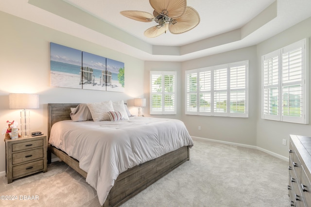 carpeted bedroom with ceiling fan and a tray ceiling