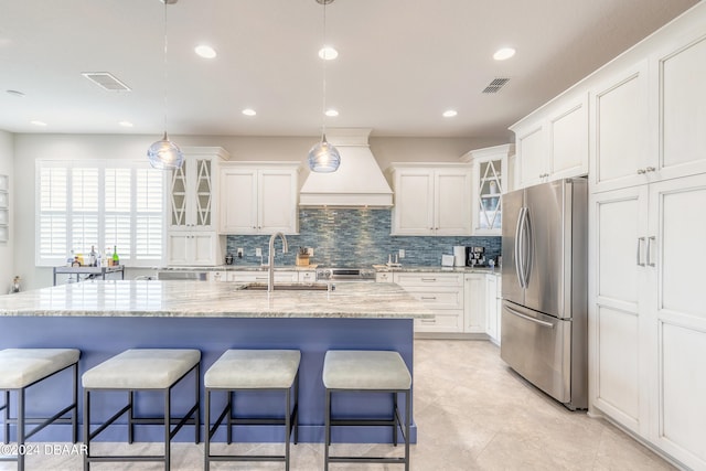 kitchen with stainless steel fridge, white cabinetry, sink, and a kitchen island with sink