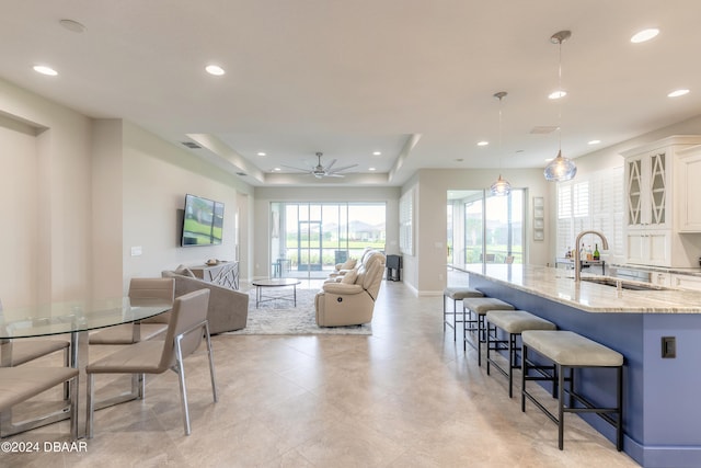 interior space featuring white cabinets, hanging light fixtures, sink, a kitchen breakfast bar, and light stone countertops