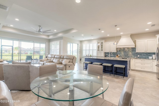 dining area featuring light tile patterned floors, ceiling fan, sink, and a tray ceiling