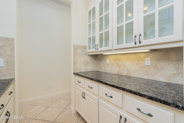 kitchen with light tile patterned floors, dark stone countertops, tasteful backsplash, and glass insert cabinets