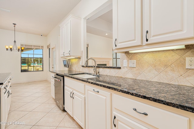 kitchen with a sink, dark stone countertops, light tile patterned floors, decorative backsplash, and a chandelier