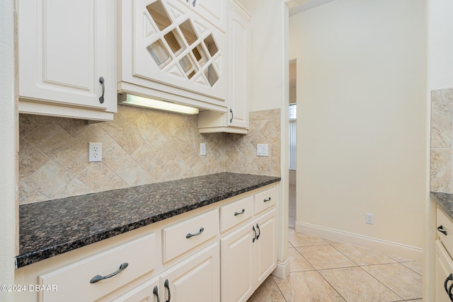 kitchen featuring light tile patterned floors, baseboards, dark stone counters, white cabinetry, and backsplash