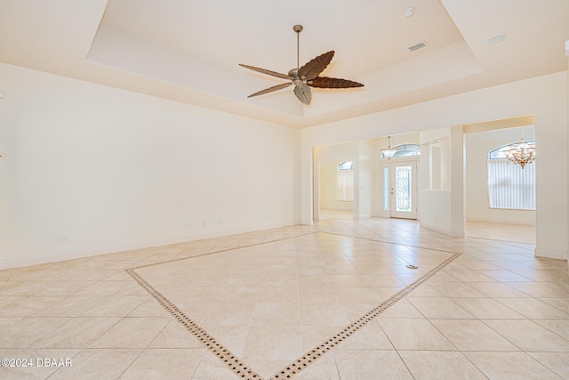 empty room featuring light tile patterned floors, visible vents, baseboards, and a tray ceiling