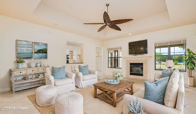 living area with a tray ceiling, light tile patterned floors, a high end fireplace, and ceiling fan