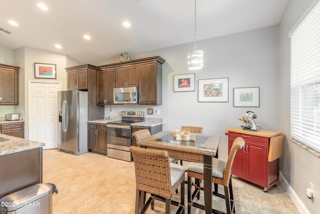 kitchen with a healthy amount of sunlight, hanging light fixtures, light stone counters, and appliances with stainless steel finishes