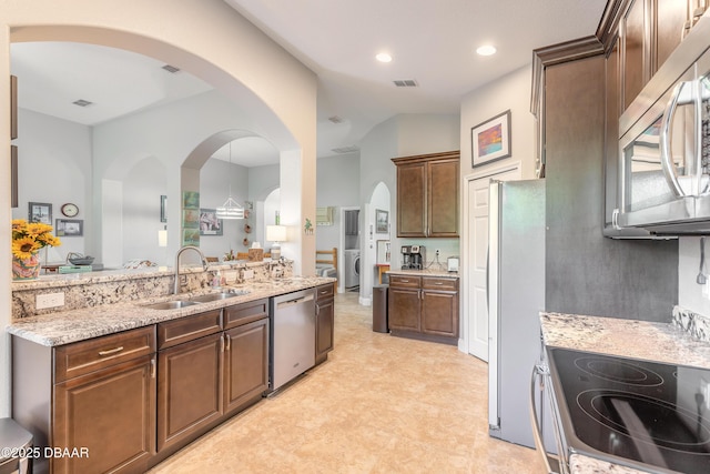 kitchen with light stone counters, dark brown cabinets, stainless steel appliances, sink, and washer / dryer