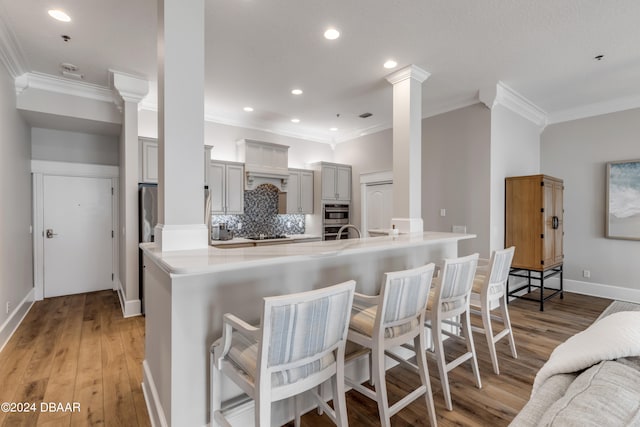 kitchen featuring ornate columns, light wood-type flooring, crown molding, and a breakfast bar