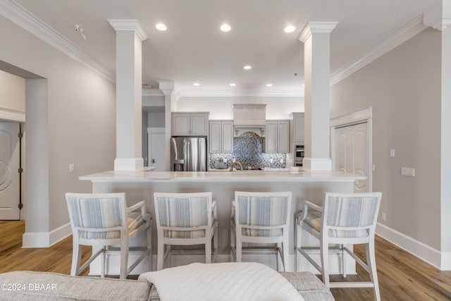 kitchen featuring stainless steel appliances, decorative columns, gray cabinetry, light wood-type flooring, and decorative backsplash