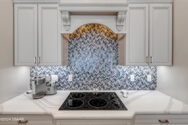 kitchen with backsplash, light stone countertops, white cabinets, and black electric stovetop