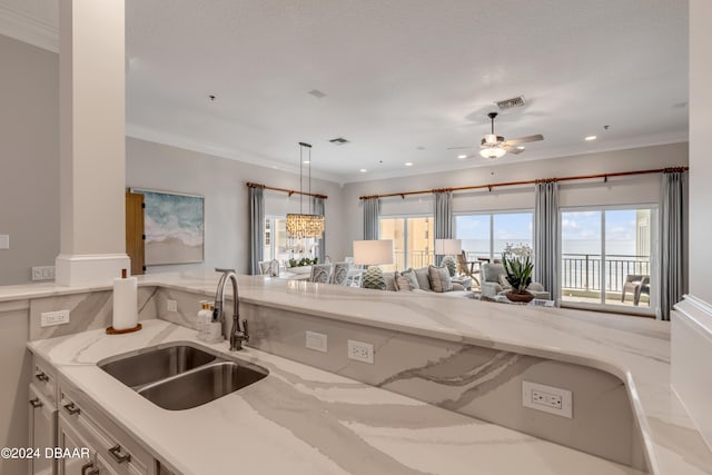 kitchen with ornamental molding, ceiling fan with notable chandelier, sink, and light stone countertops