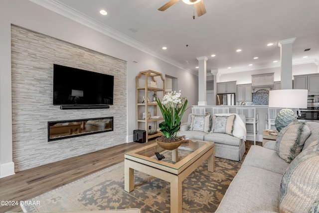 living room featuring crown molding, a fireplace, ornate columns, hardwood / wood-style floors, and ceiling fan