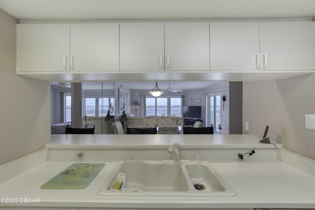 kitchen featuring a sink, open floor plan, white cabinetry, and light countertops