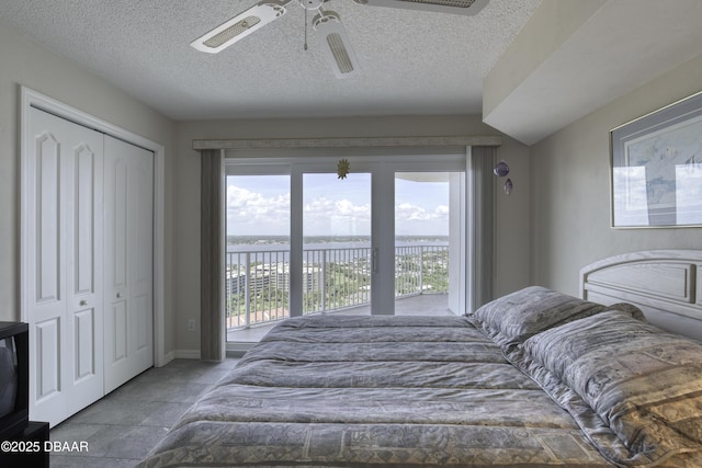 bedroom featuring a ceiling fan, a closet, a textured ceiling, a water view, and access to exterior