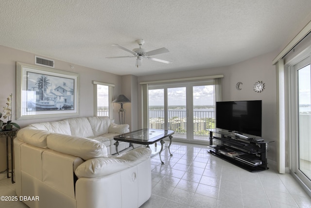 living room featuring light tile patterned floors, a textured ceiling, visible vents, and a ceiling fan