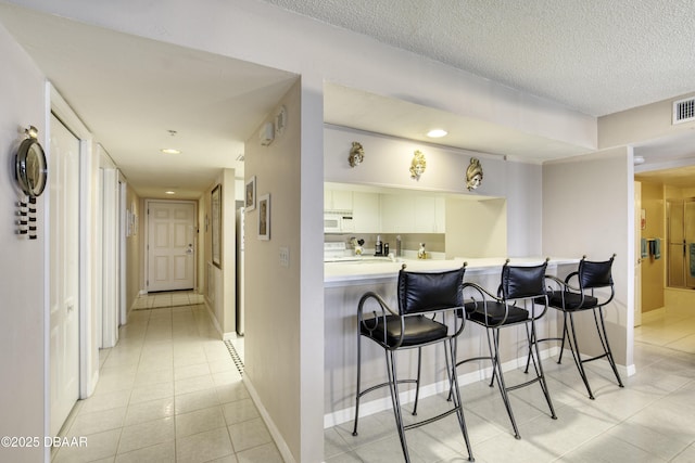 bar featuring light tile patterned floors, baseboards, white microwave, and visible vents