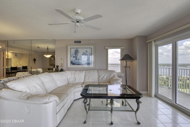living room with a textured ceiling, visible vents, a ceiling fan, light tile patterned floors, and a water view