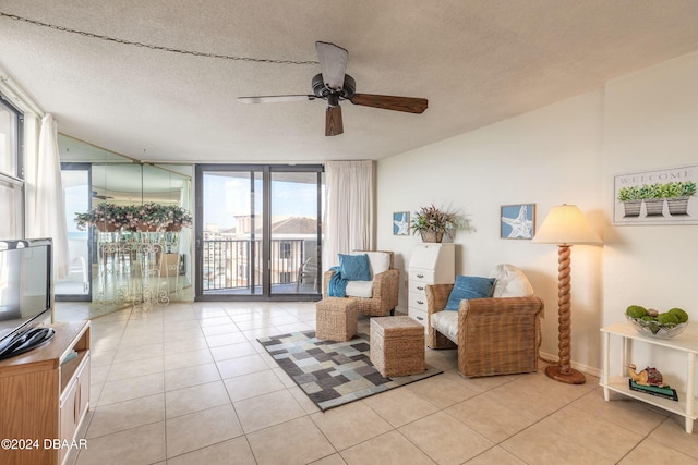 living area featuring ceiling fan, light tile patterned floors, a textured ceiling, and a wall of windows