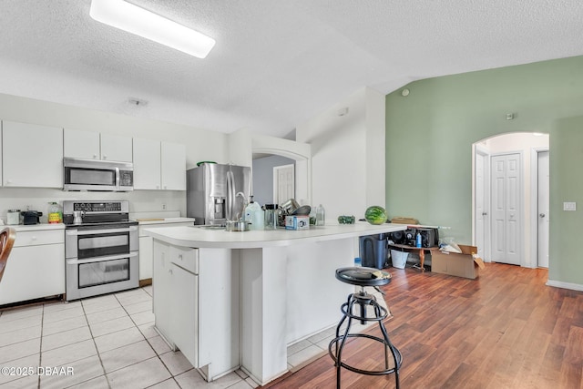 kitchen with white cabinets, a kitchen breakfast bar, arched walkways, light countertops, and appliances with stainless steel finishes