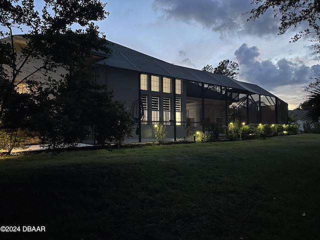 back house at dusk featuring a yard and glass enclosure