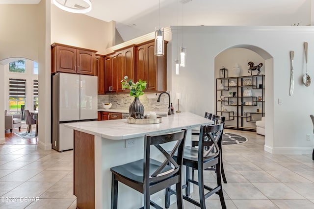 kitchen with light tile patterned floors, a peninsula, arched walkways, freestanding refrigerator, and a kitchen breakfast bar