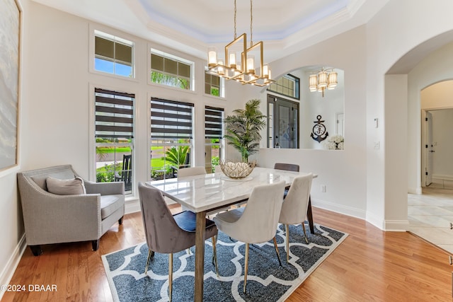 dining area with wood-type flooring, ornamental molding, a notable chandelier, and a tray ceiling