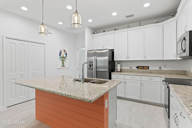 kitchen with appliances with stainless steel finishes, a kitchen island with sink, white cabinets, and decorative light fixtures