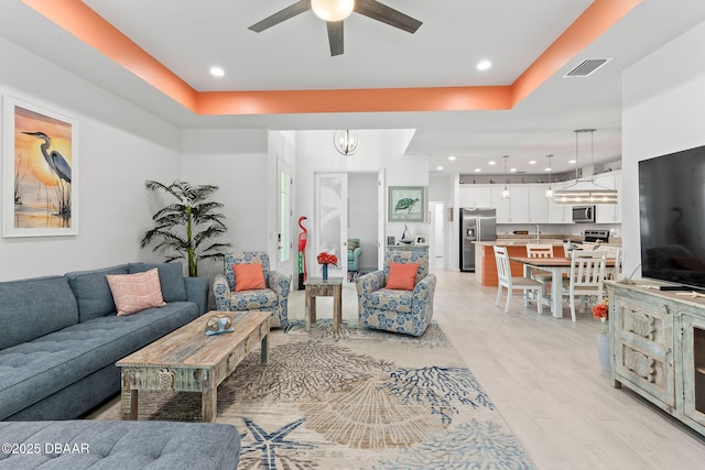 living room with a tray ceiling, ceiling fan with notable chandelier, and light hardwood / wood-style floors