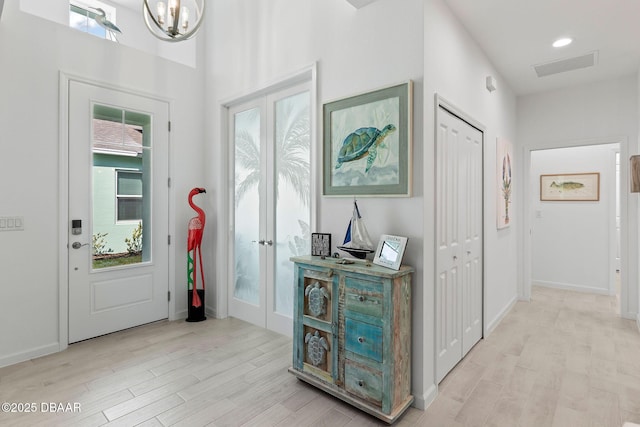 entryway with an inviting chandelier, light hardwood / wood-style floors, and french doors