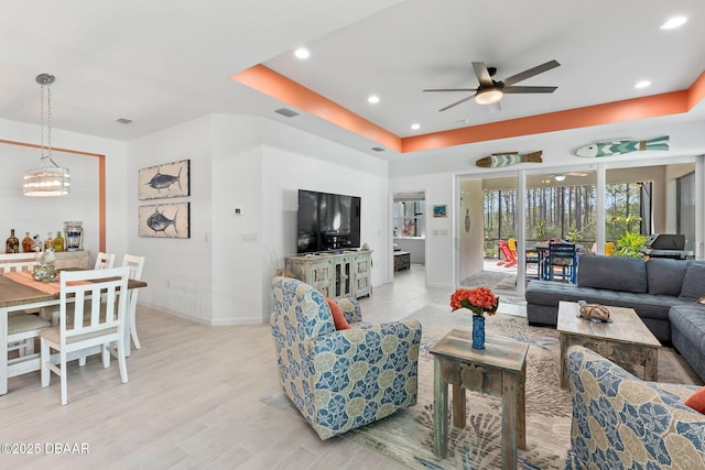 living room with light hardwood / wood-style flooring, ceiling fan, and a tray ceiling