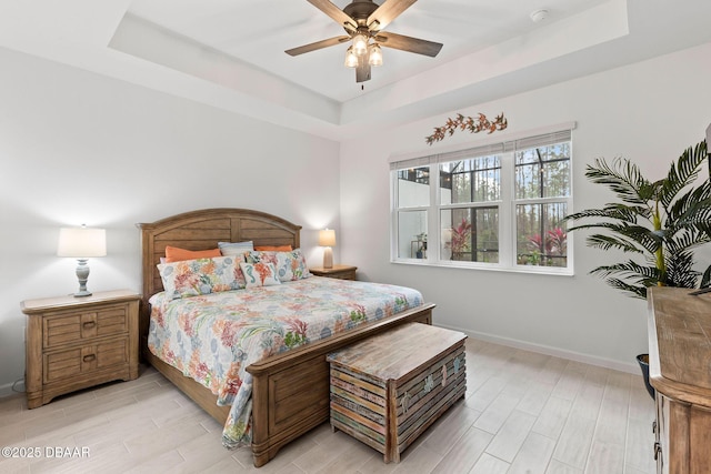 bedroom with ceiling fan, a raised ceiling, and light hardwood / wood-style floors