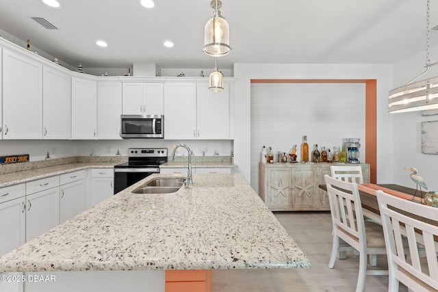 kitchen featuring sink, hanging light fixtures, stainless steel appliances, a kitchen island with sink, and white cabinets