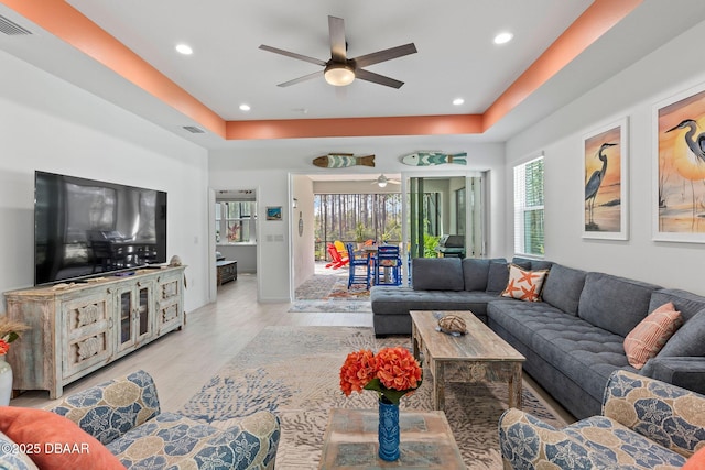 living room featuring ceiling fan, light hardwood / wood-style floors, and a tray ceiling