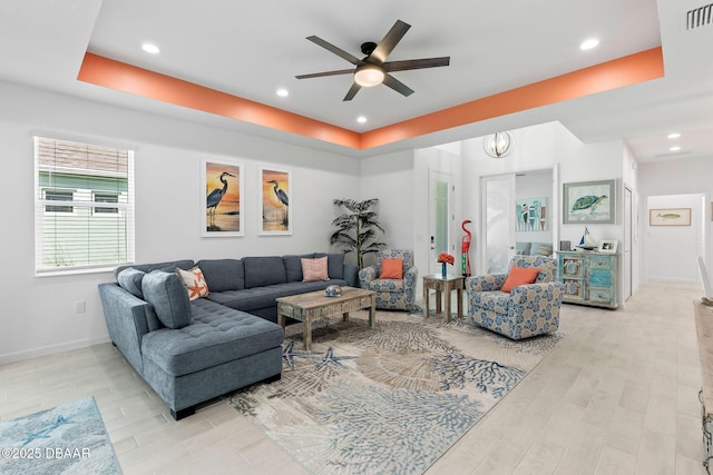 living room with a raised ceiling, ceiling fan, and light hardwood / wood-style floors