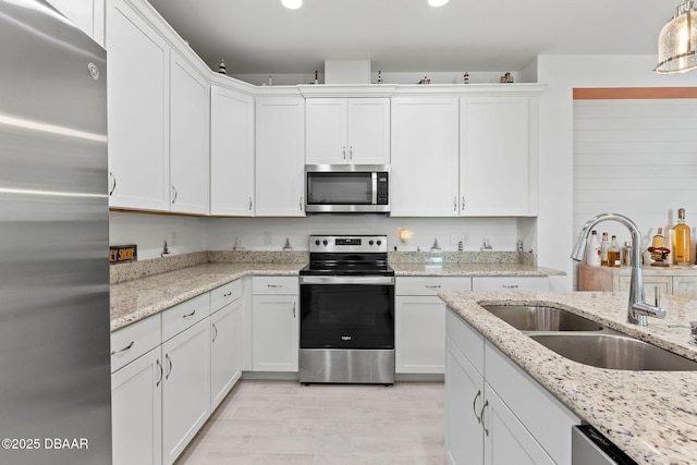 kitchen featuring white cabinetry, sink, hanging light fixtures, stainless steel appliances, and light stone countertops