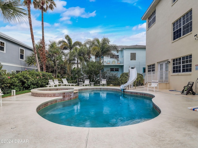 view of pool with a water slide, an in ground hot tub, and a patio area