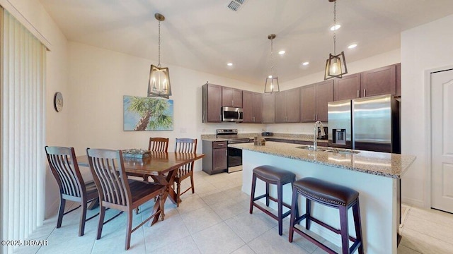 kitchen with decorative light fixtures, a breakfast bar area, an island with sink, appliances with stainless steel finishes, and a sink