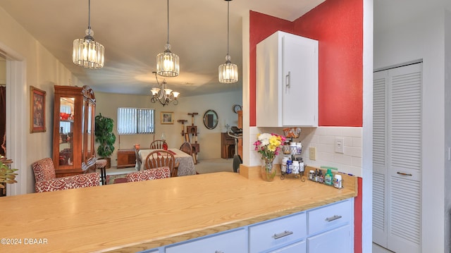 kitchen featuring white cabinetry, decorative backsplash, a notable chandelier, and hanging light fixtures